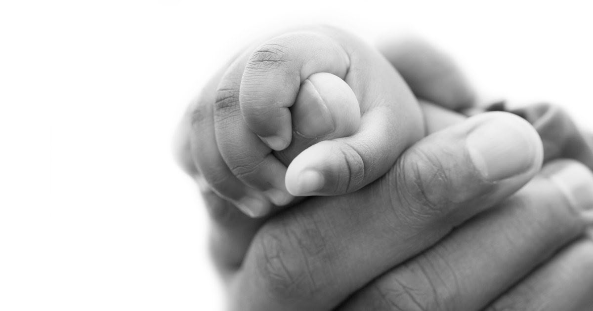 Black and white close-up of a small hand resting within a larger, supportive hand